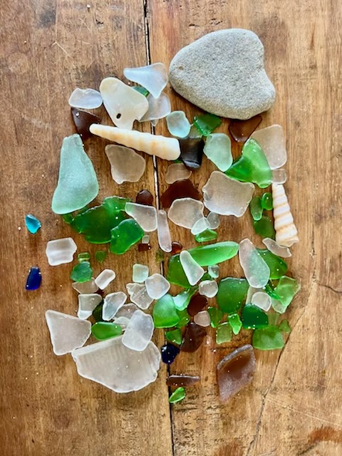 A personal collection of sea glass, shells and a smooth stone on a wooden surface