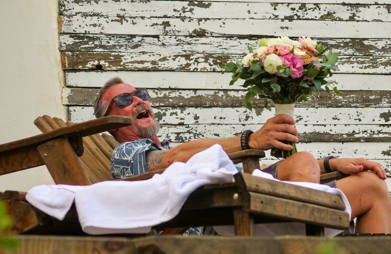 Warren laughing in a wooden chair while holding a bouquet of flowers